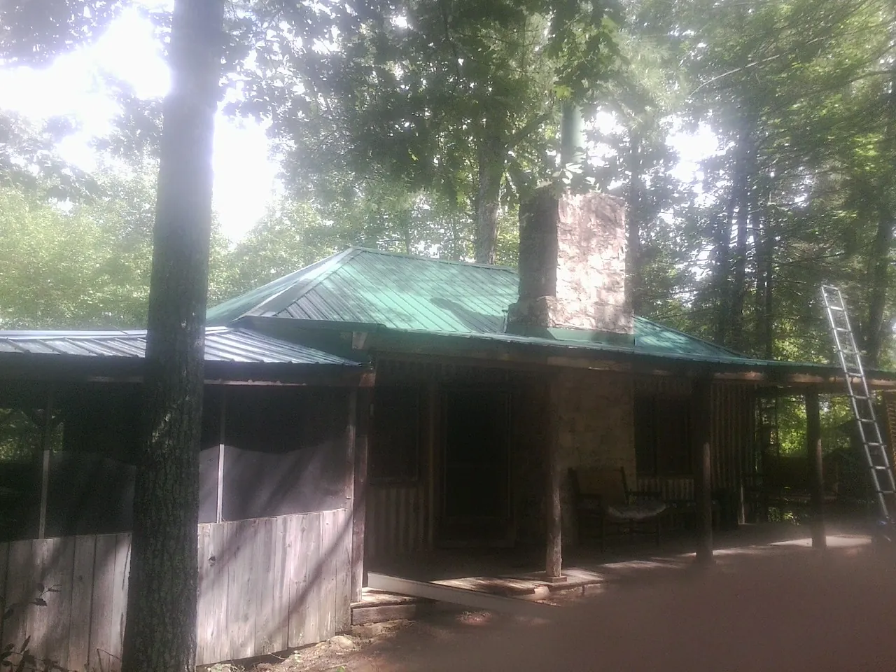 Green metal roof and stone chimney above a log cabin porch in Waverly