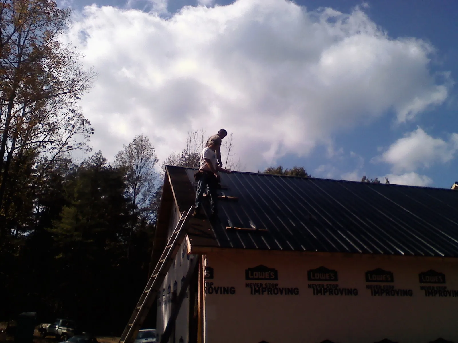 Roofer fastening dark metal panels high against a cloudy sky, from a Roof Inspection job in Waverly