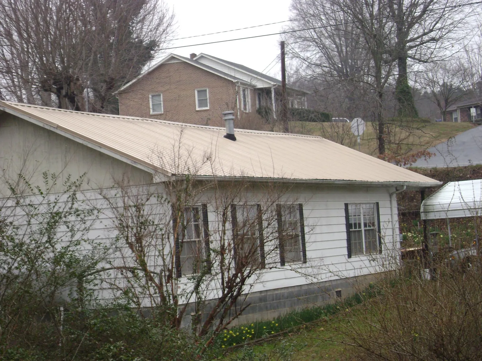 Tan metal roof on a white sided house set into a hillside — Commercial Roofing by Roofing Brothers in Waverly